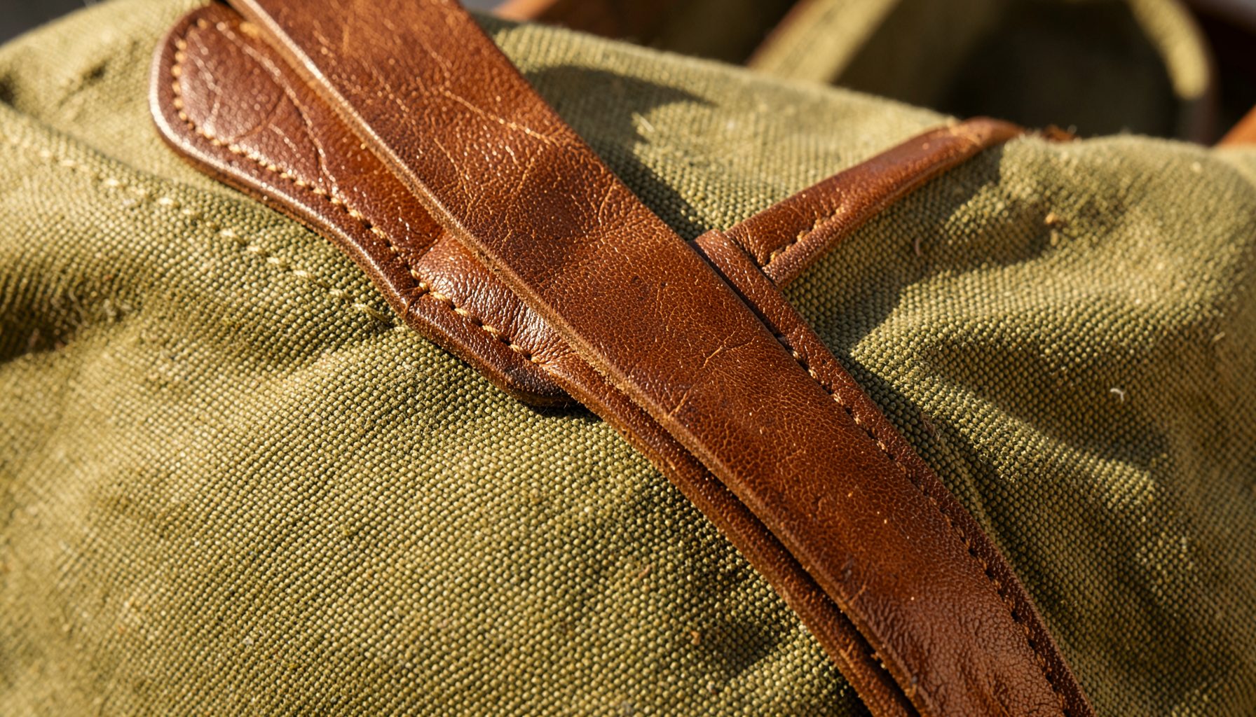 A close-up detail of Horween Chromexcel leather trim meeting waxed canvas on a tote bag, showing the rich brown leather grain and the textured olive canvas in warm daylight.