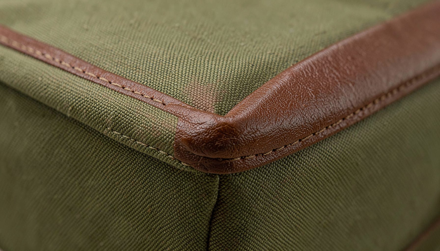 A close-up of a waxed canvas dopp kit corner showing the rich texture of Horween Chromexcel leather trim against tightly woven olive canvas.