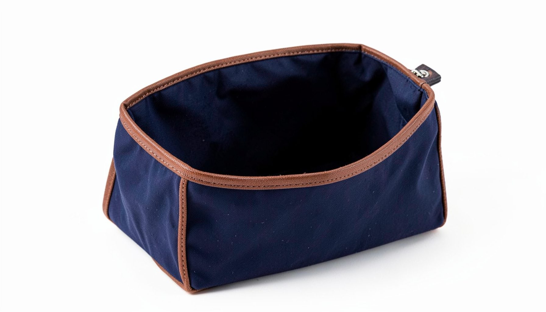 A generously sized toiletry bag in navy waxed canvas with brown leather trim, open to show a spacious interior.