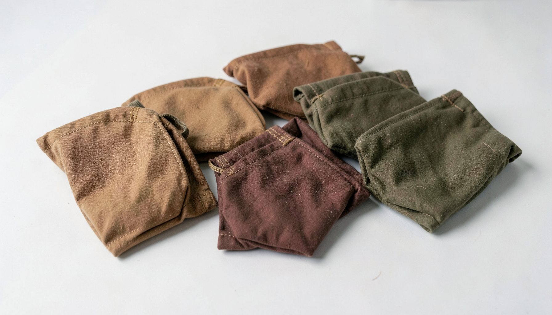 A set of small waxed canvas pouches in earthy tones, neatly arranged on a clean surface.