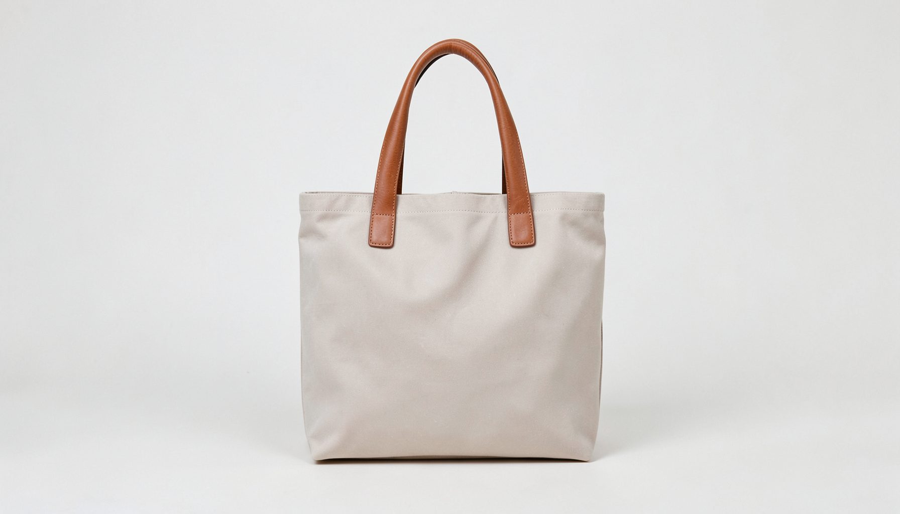 A waxed canvas tote handbag with leather handles in a soft neutral tone, photographed against a light background