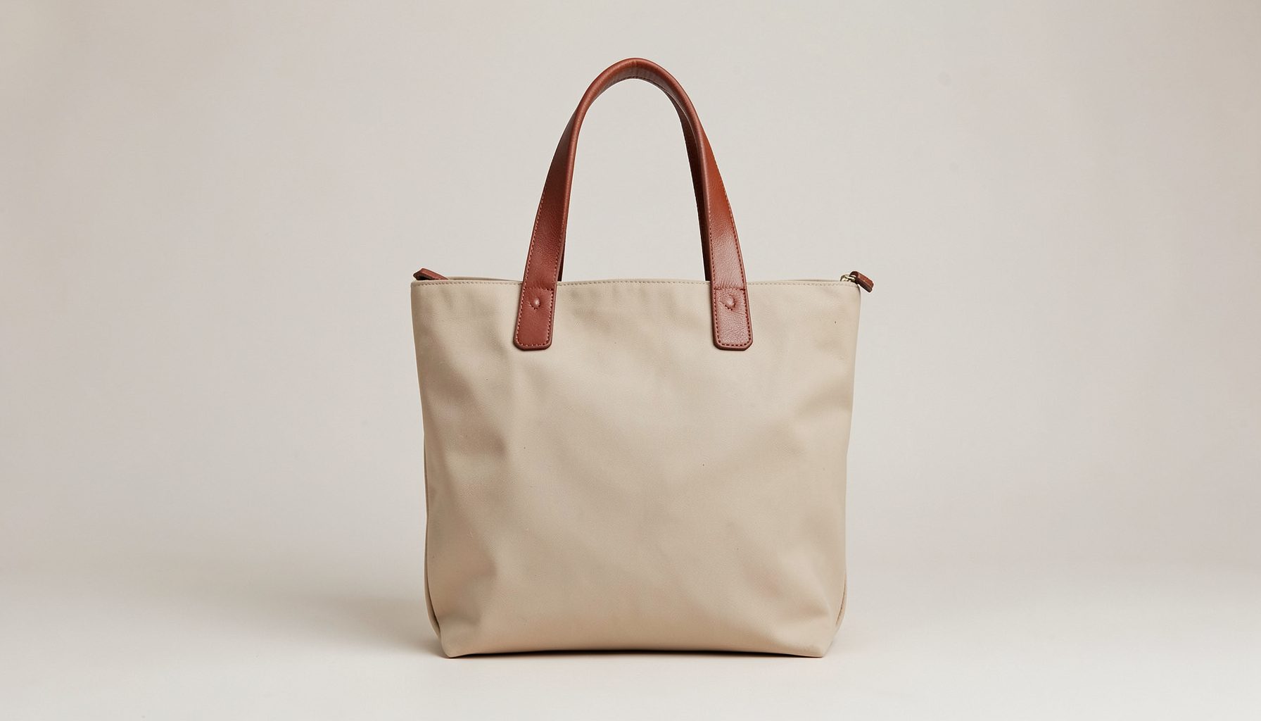 A waxed canvas tote handbag with leather handles, set against a soft neutral background.