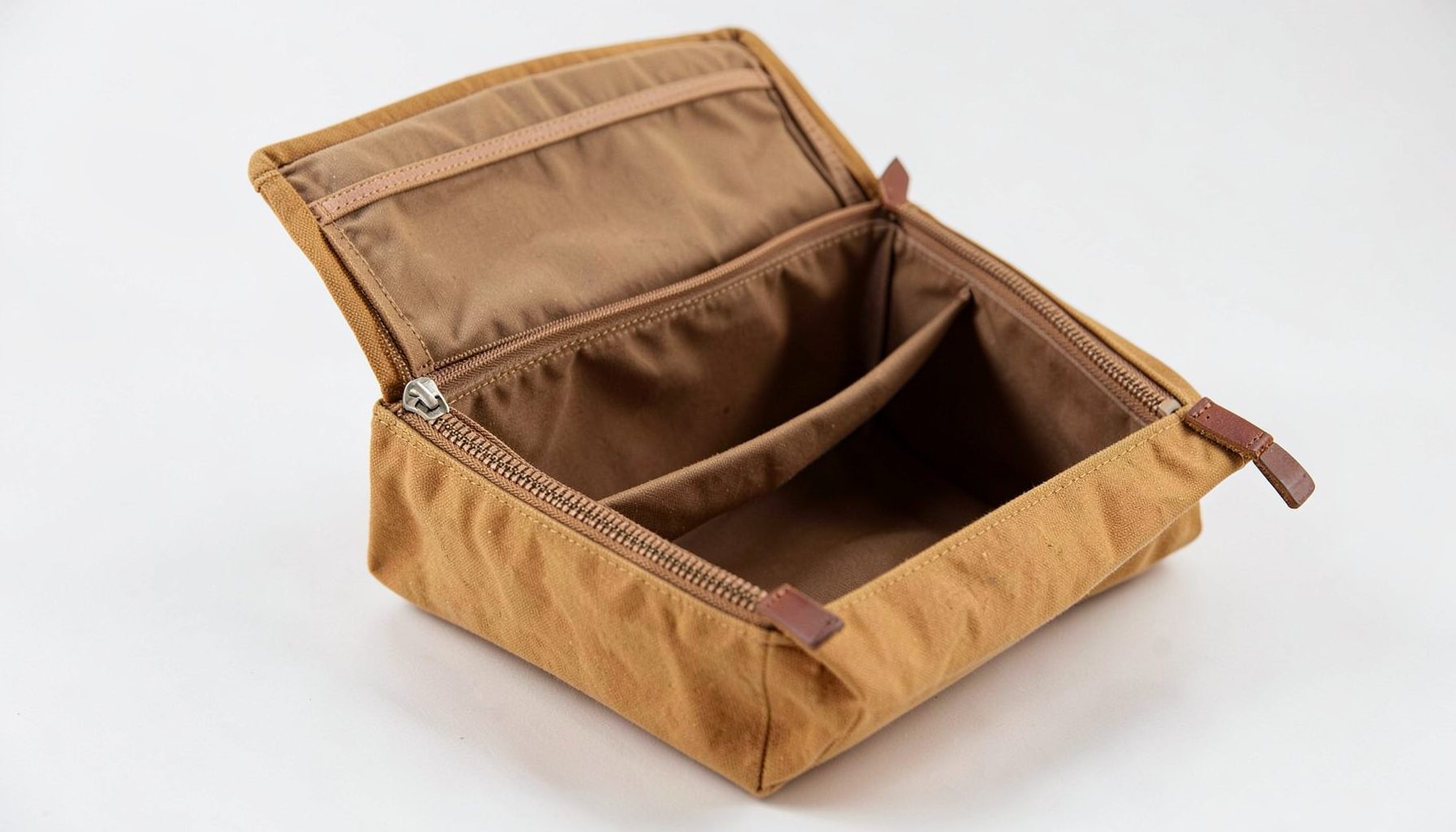 An expandable dopp kit in tan waxed canvas, shown open and revealing its extended capacity, with leather zipper pulls visible.